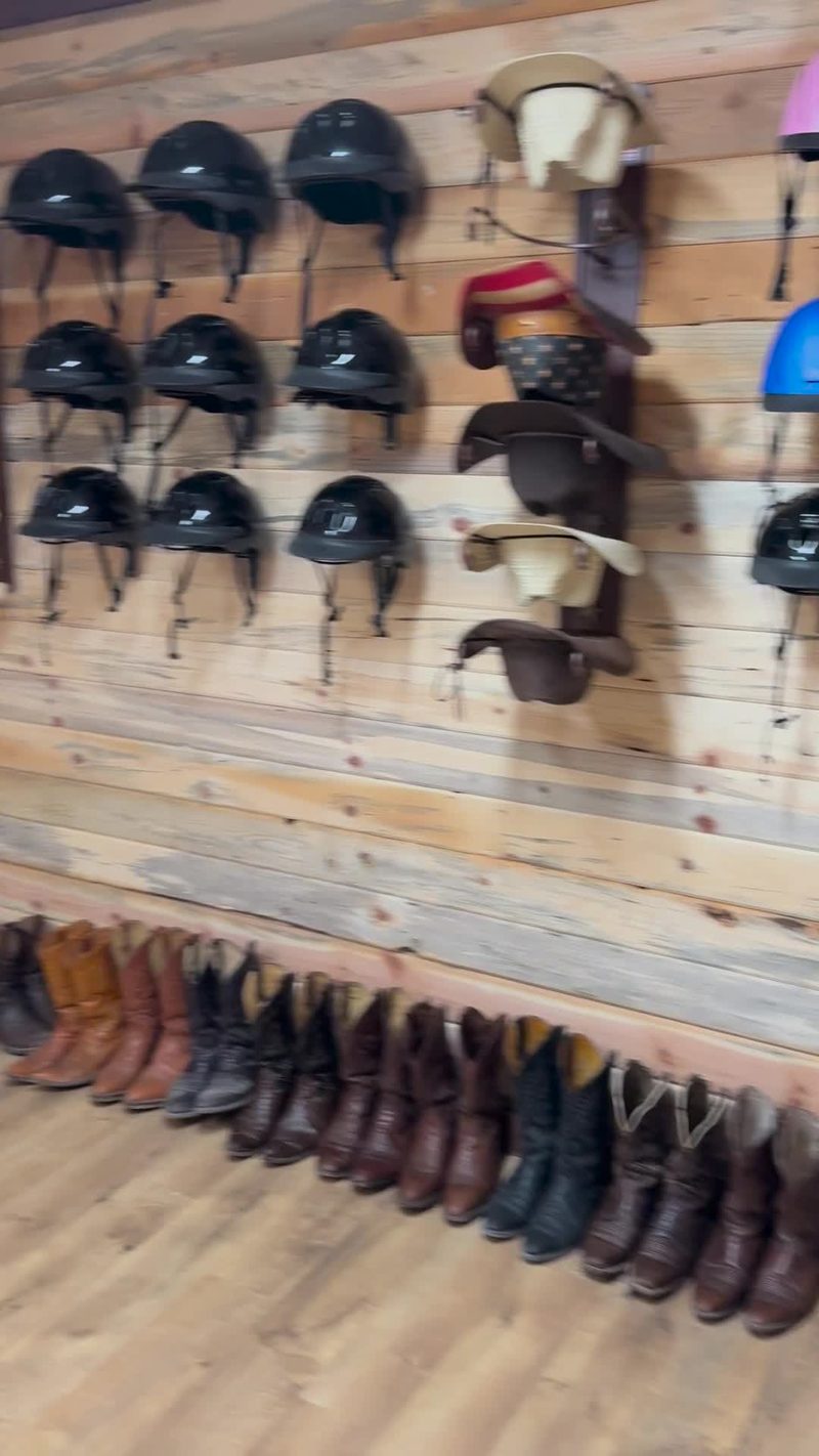 Wall of riding helmets and cowboy hats above a row of loaner cowboy boots
