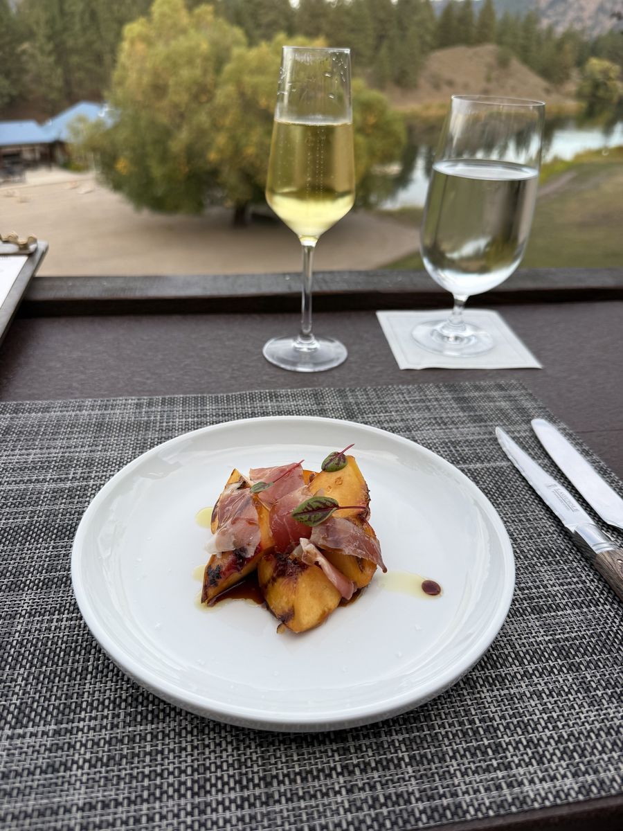 Grilled peaches with speck ham on a white plate, with the lake in the background